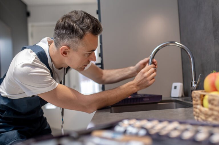 Man leaning over water faucet touching pipe